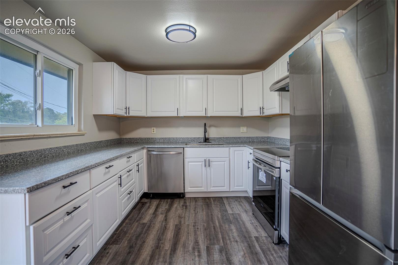 Kitchen featuring white shaker-style cabinetry, stone-finish countertops, stainless steel appliances, and wood-finish flooring