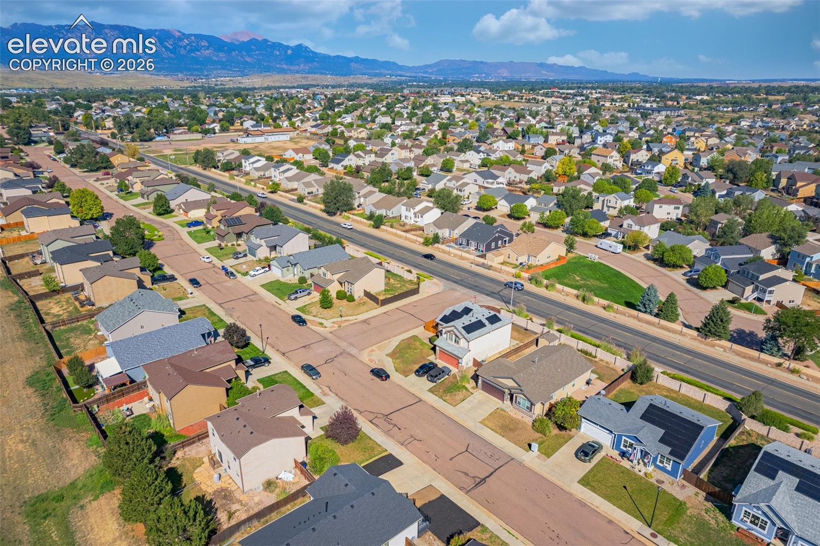 Residential neighborhood featuring a paved street, mature trees, and mountain backdrop