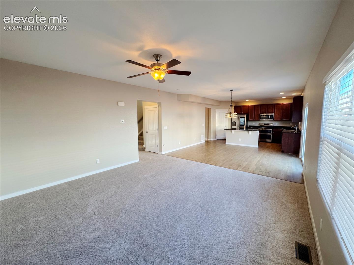 Living area featuring neutral carpeting and a ceiling fan, kitchen with dark-finish cabinetry, a central island, and wood-finish flooring