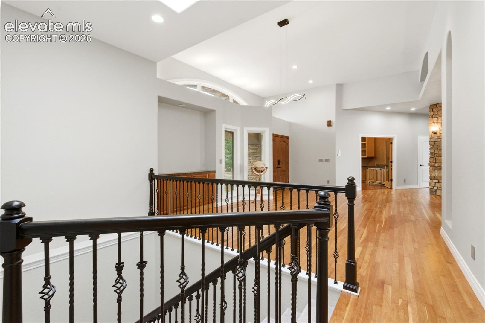 Hardwood flooring, wrought iron railing, vaulted ceiling, recessed lighting, stone accent wall