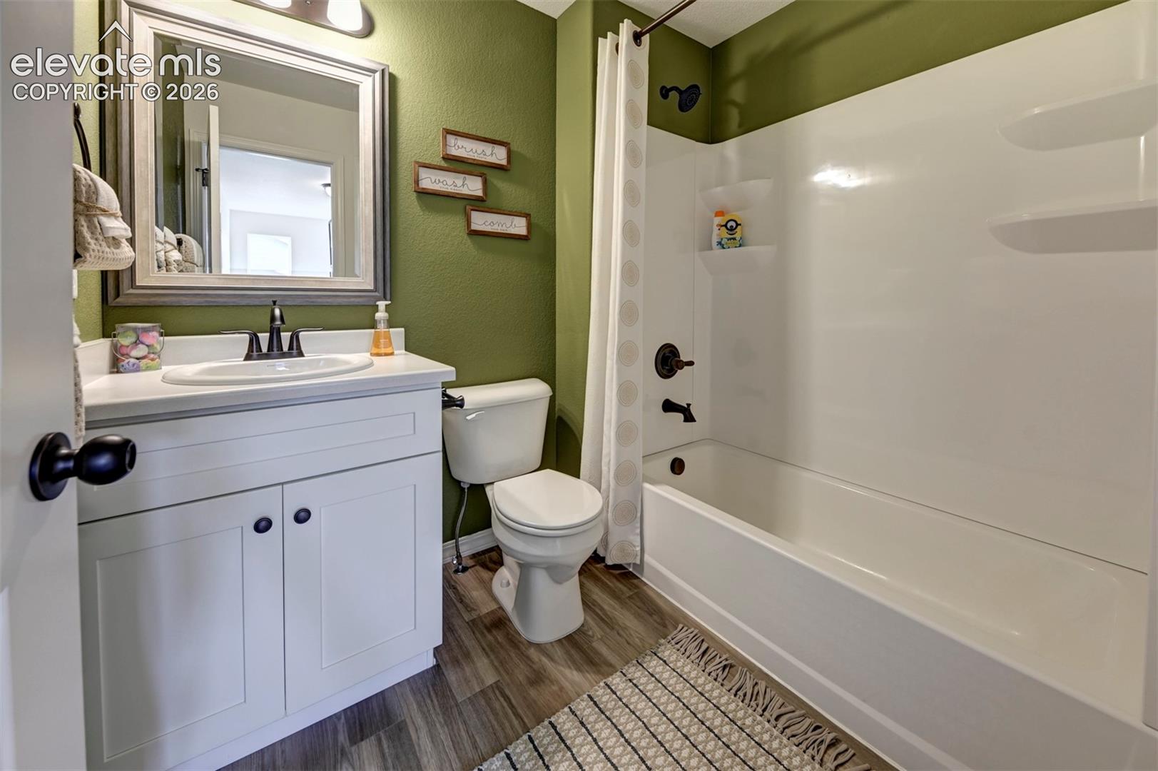 Bathroom featuring a vanity with a white cabinet and solid-surface countertop, an oval-shaped undermount sink, oil-rubbed bronze plumbing fixtures, and wood-finish flooring