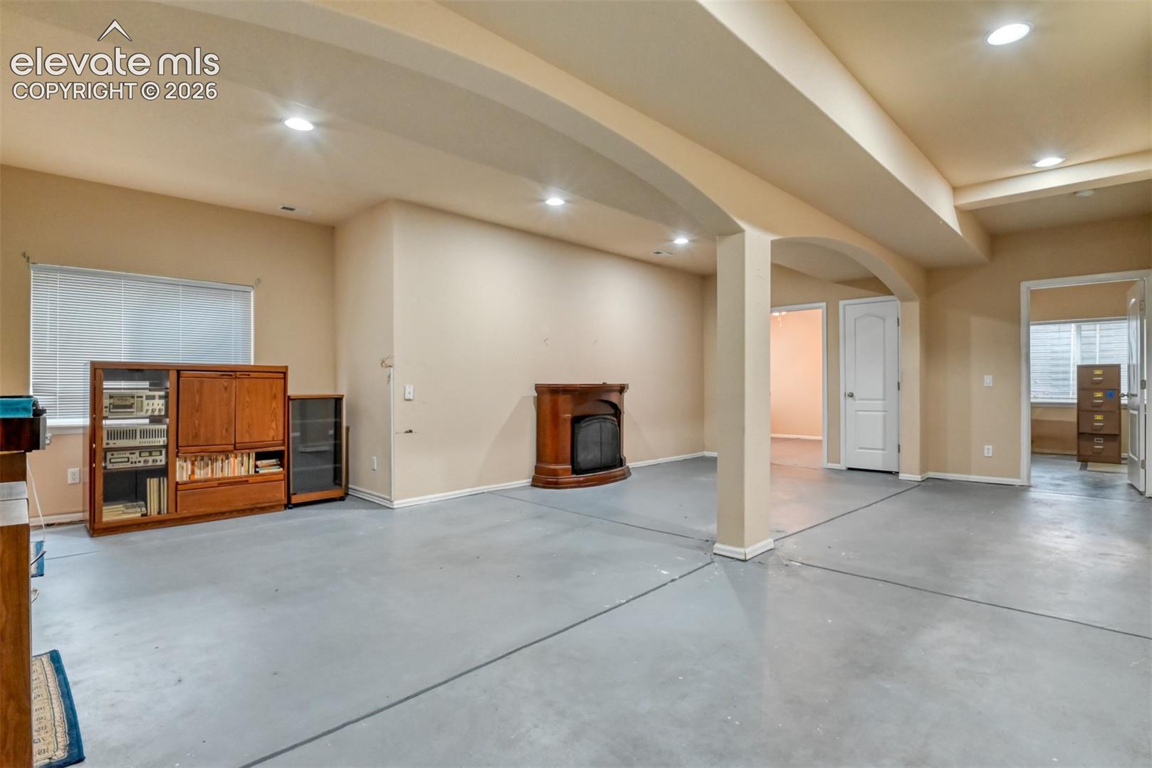 Open-concept room featuring arched structural supports, a freestanding fireplace, recessed ceiling lighting, and smooth-finish concrete flooring
