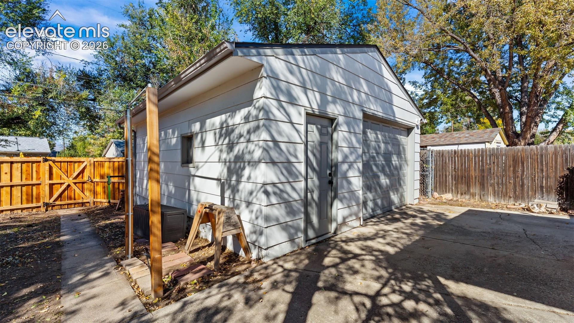 Detached two-car garage featuring white horizontal siding, a roll-up garage door, a side-entry personnel door, and concrete driveway apron
