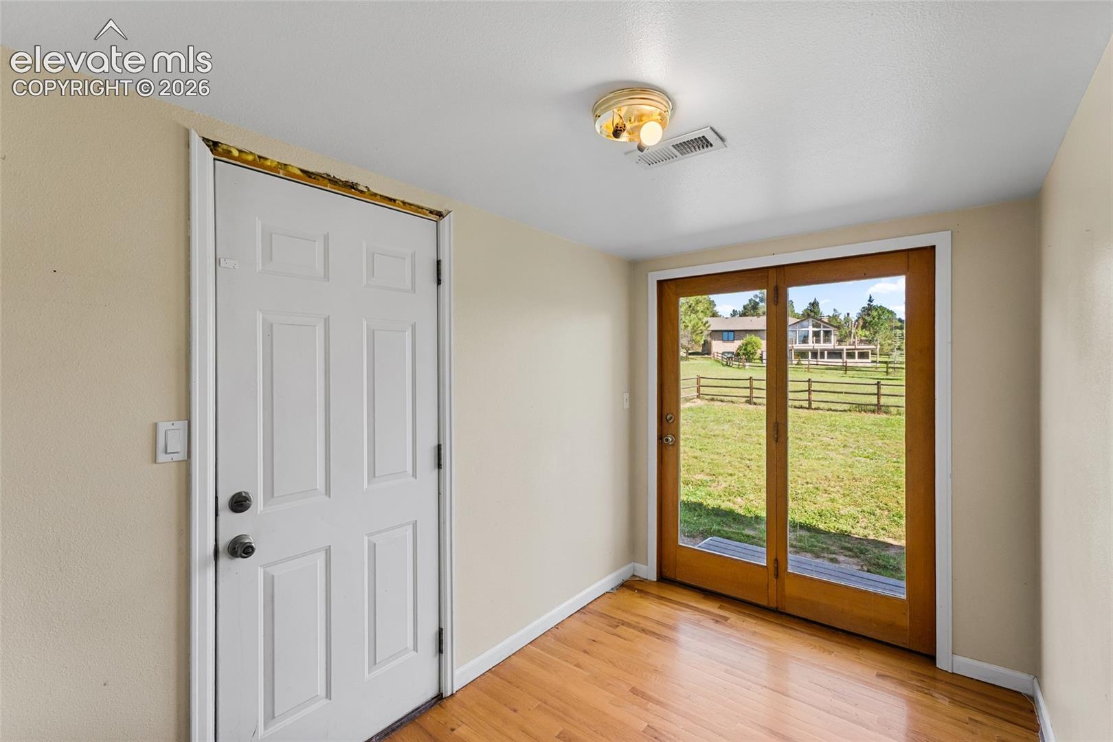 Hardwood flooring, painted interior walls, flush mount ceiling fixture, paneled door, and wood-framed glass double doors