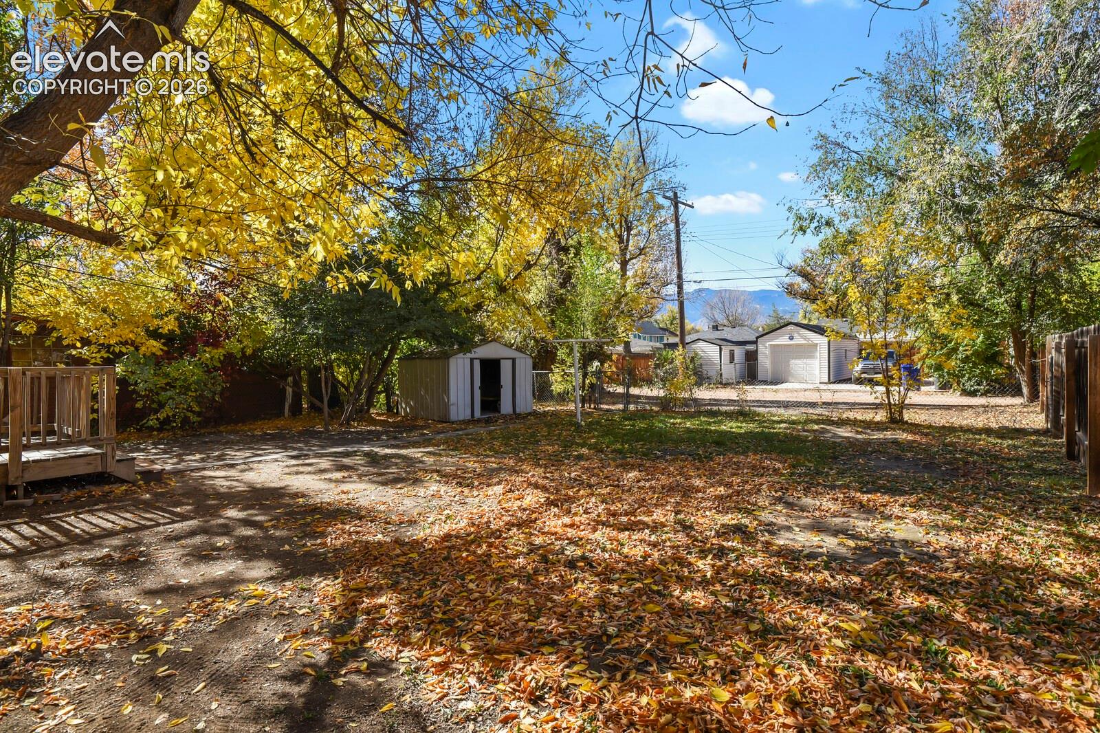 Backyard featuring mature trees, a detached storage shed, a wood-deck platform, and mountain backdrop