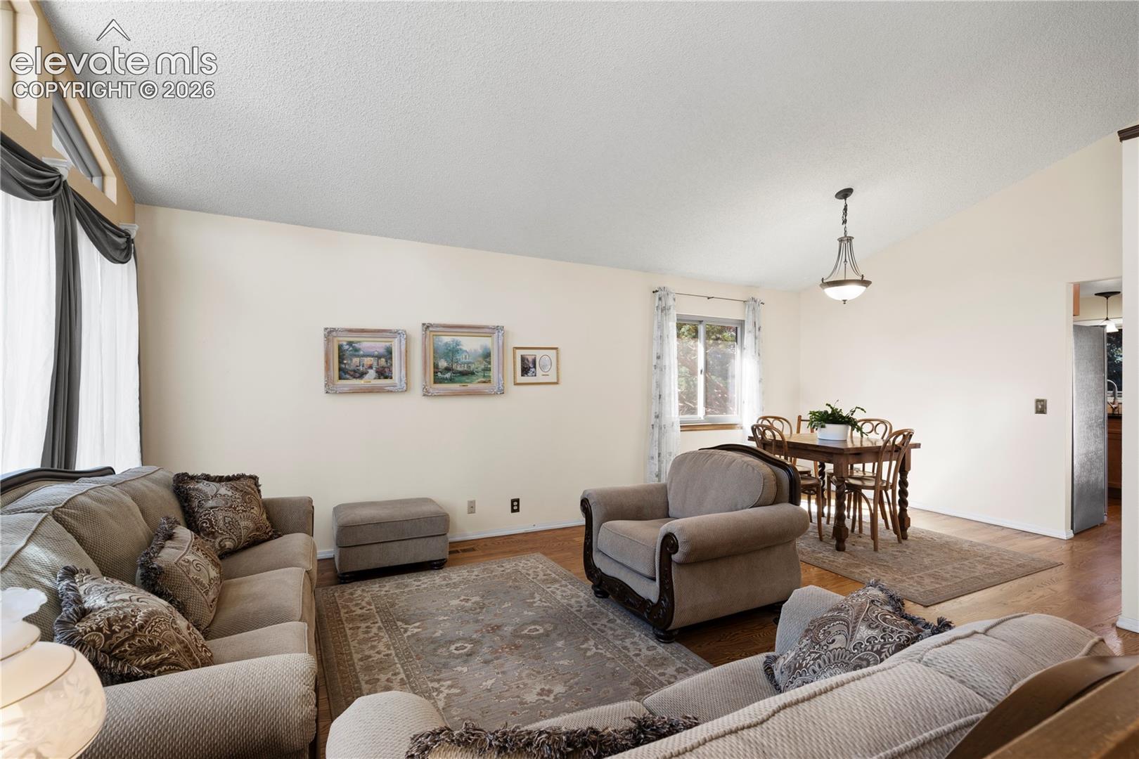 Vaulted ceiling with a decorative chandelier, wood-finish flooring, and ample natural light through a large window