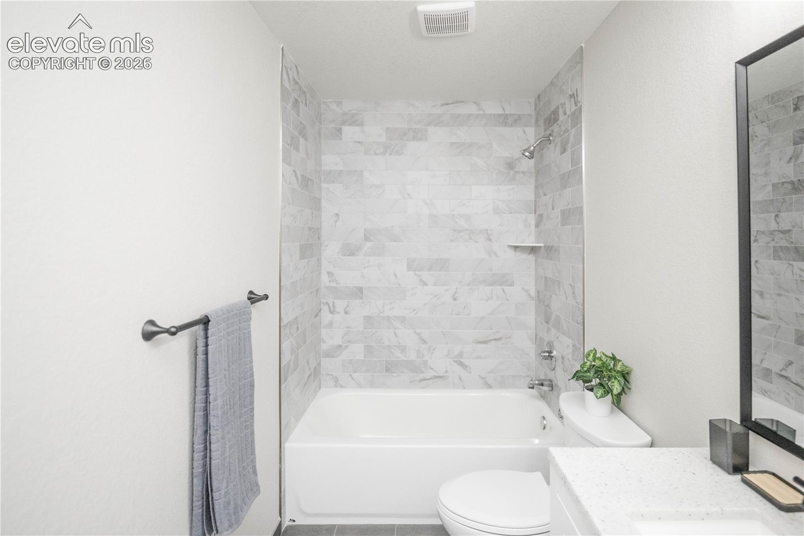 Bathroom featuring a tub-shower combination with rectangular stone-finish wall tile, white vanity with quartz countertop, and matte black fixtures