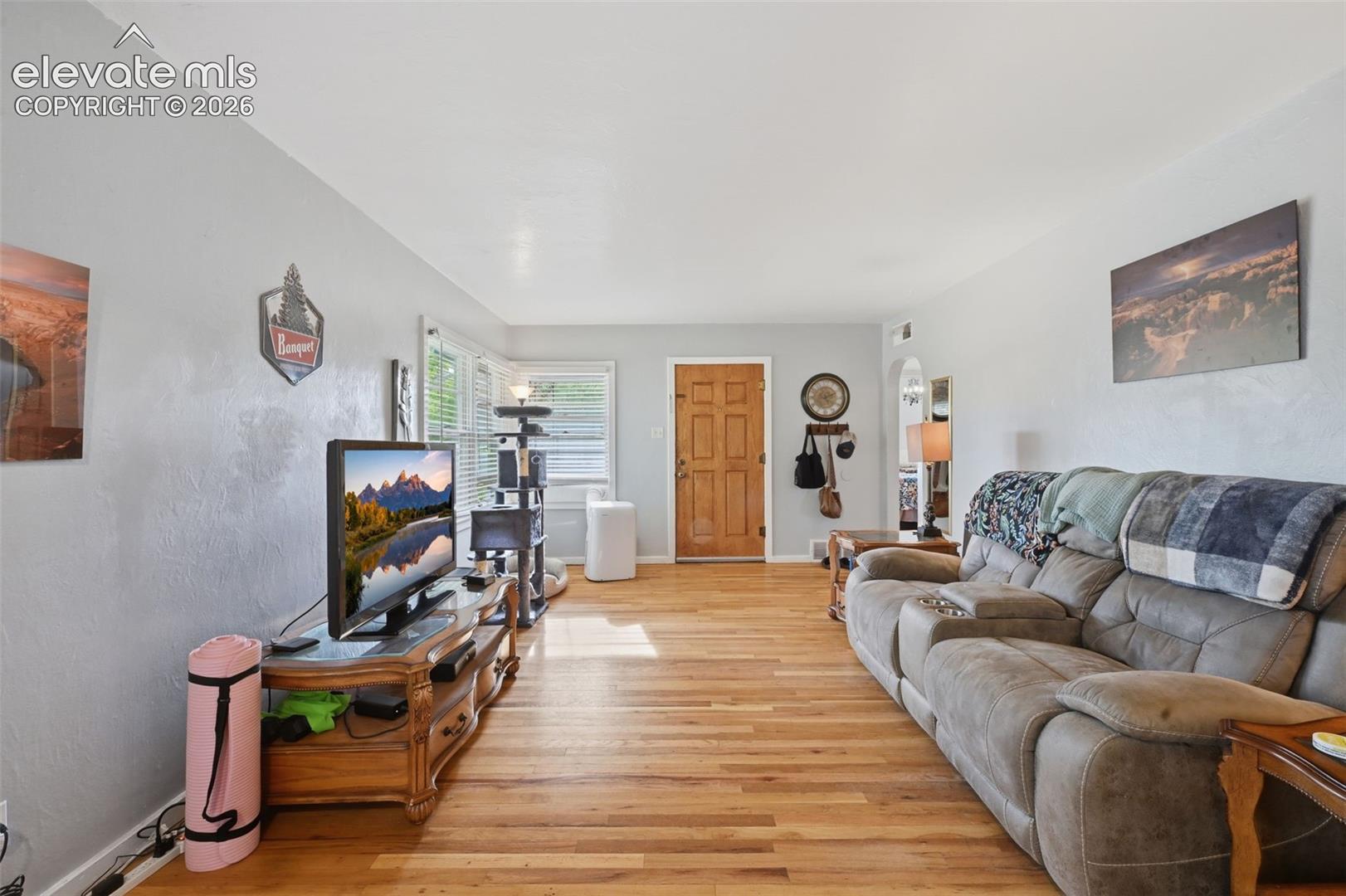 Light-toned wood-finish flooring, light grey wall paint, and a paneled wooden entry door