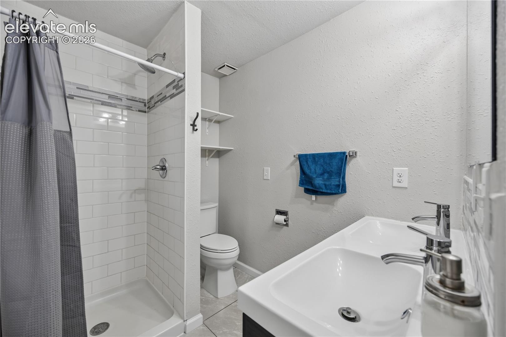 Bathroom featuring a dual-sink vanity, walk-in shower with white subway tile surround, decorative mosaic tile inlay, and built-in wall shelving