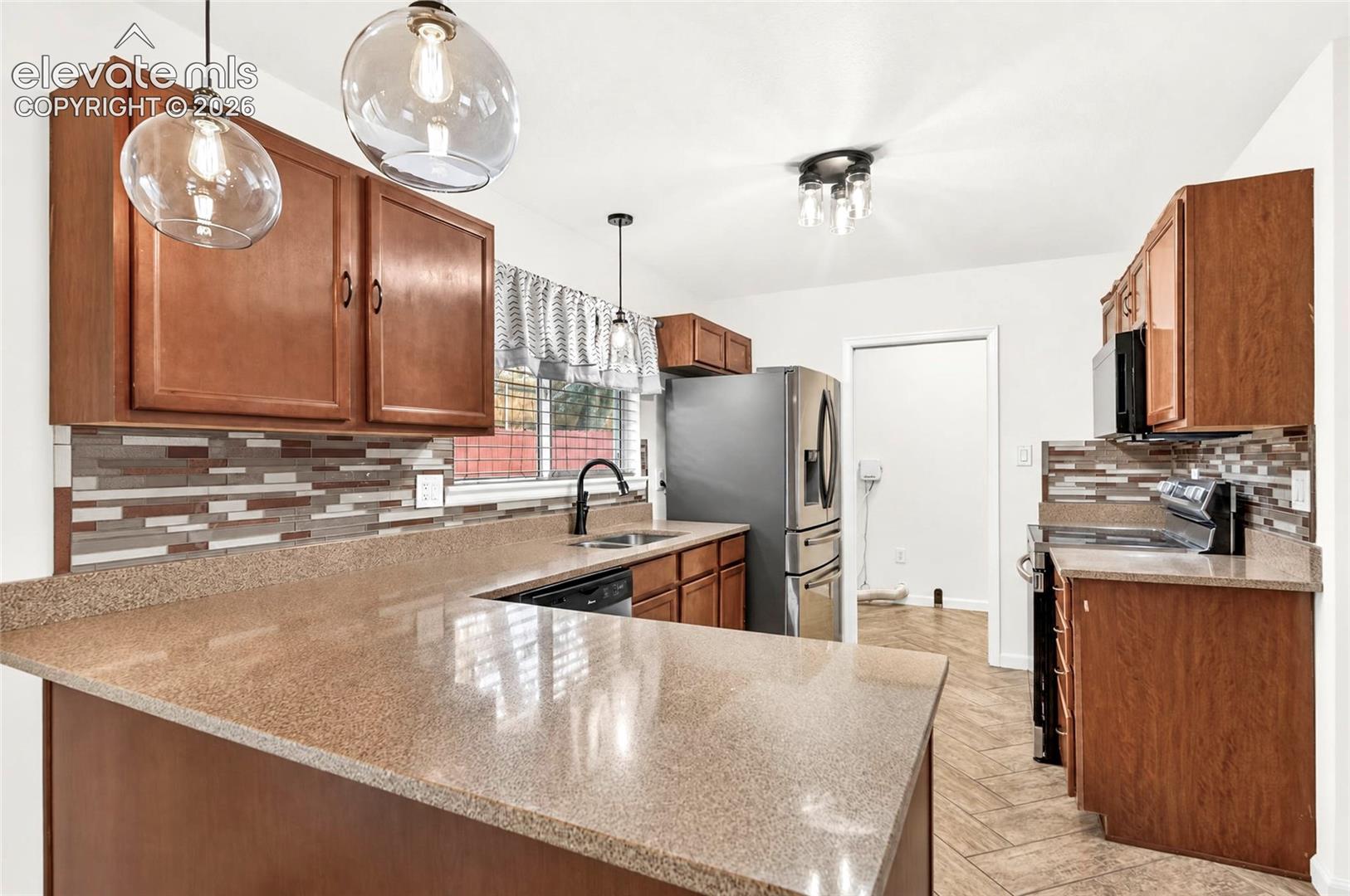 Kitchen featuring wood cabinetry, stone-finish countertops, tile backsplash, stainless steel appliances, and pendant lighting