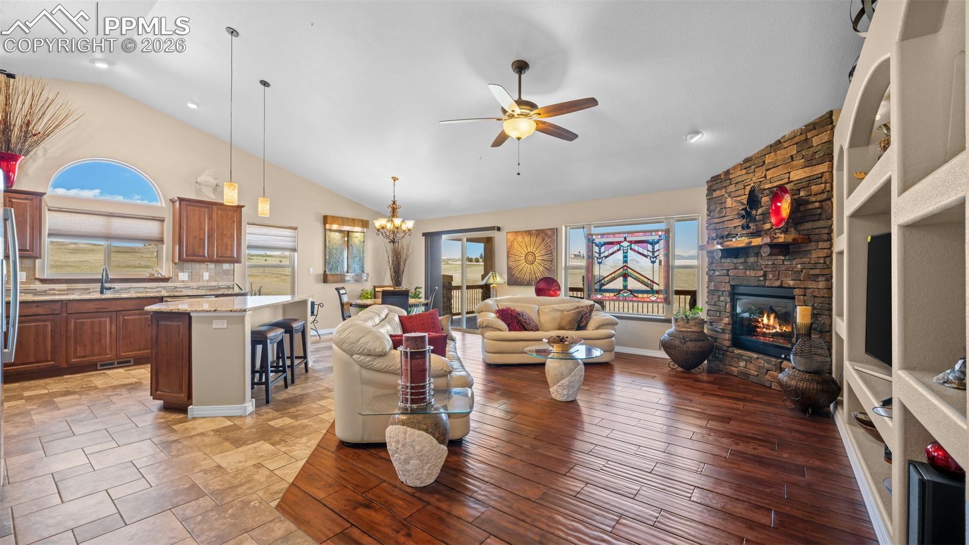 Living area with vaulted ceiling, a ceiling fan, suspended lighting, and a fireplace