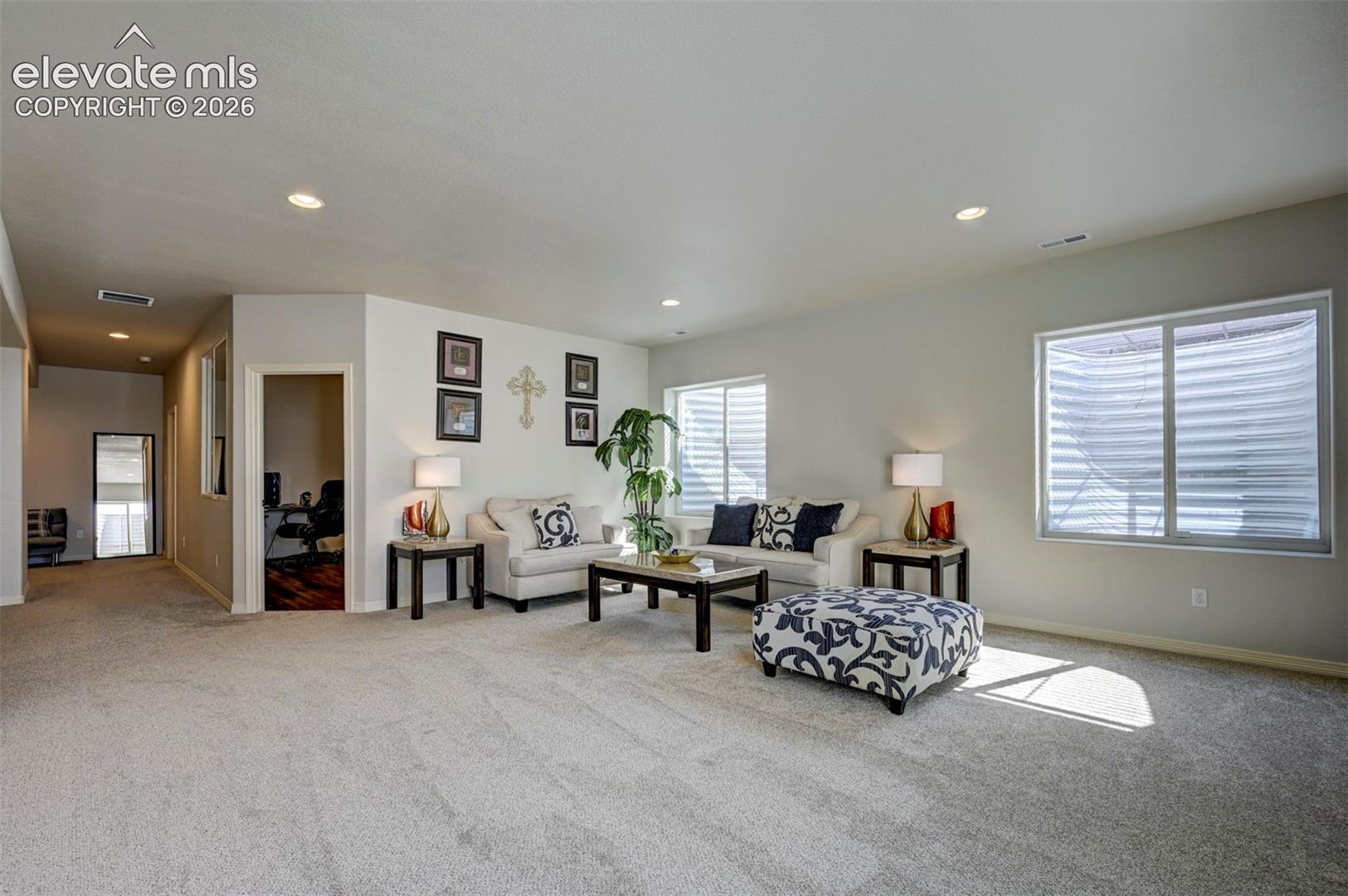 Spacious interior room featuring light-colored carpeting, recessed lighting, and multiple windows
