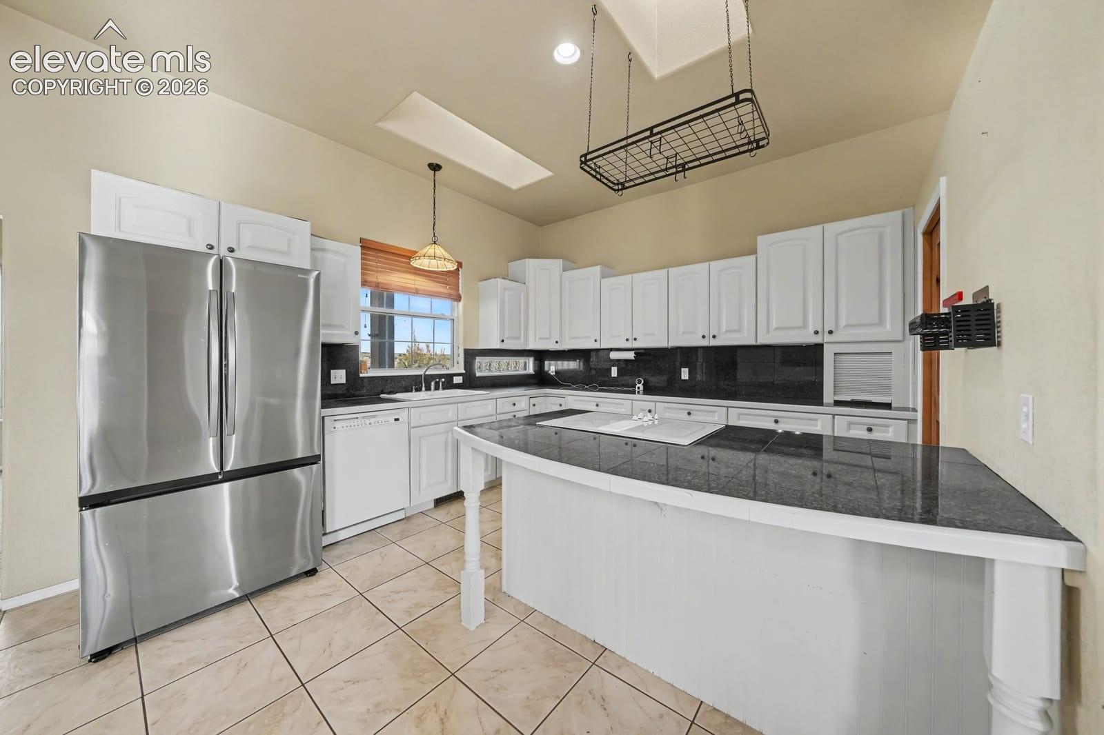 Kitchen featuring white cabinetry, dark stone countertops, stainless steel refrigerator, recessed lighting, and a skylight