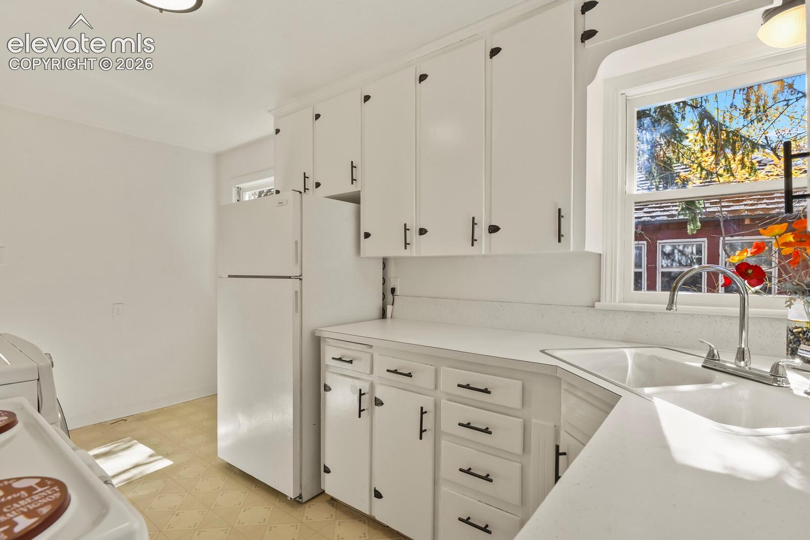 White cabinetry featuring matte black hardware, solid surface countertops, dual-basin under-mount sink, and arched window
