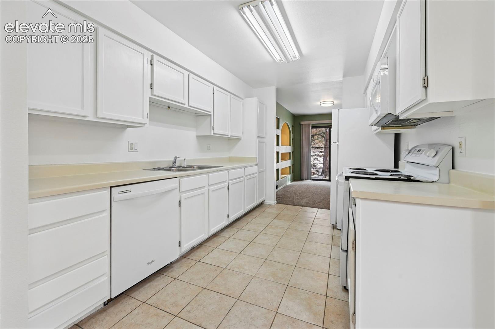 Galley kitchen featuring white cabinetry, light-toned countertops, a stainless steel sink, a white dishwasher, and tiled flooring