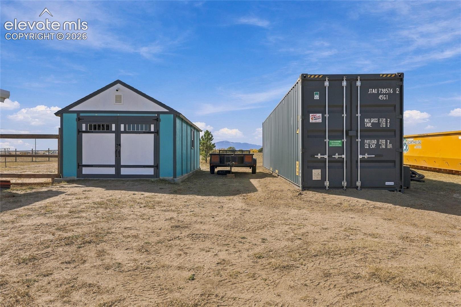 Exterior storage structures featuring a gable-roof shed with double entry doors and a detached metal shipping container