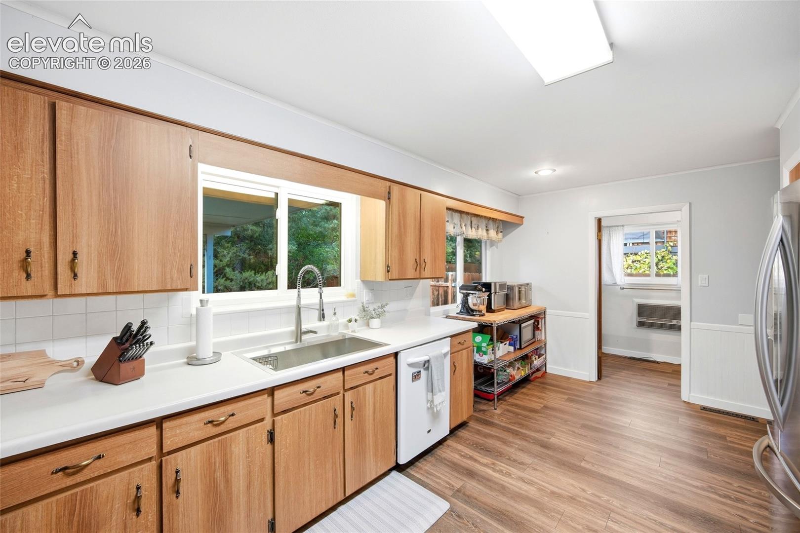 Kitchen featuring wood-finish cabinetry, solid surface countertops, stainless steel undermount sink with gooseneck faucet, and wood-finish flooring