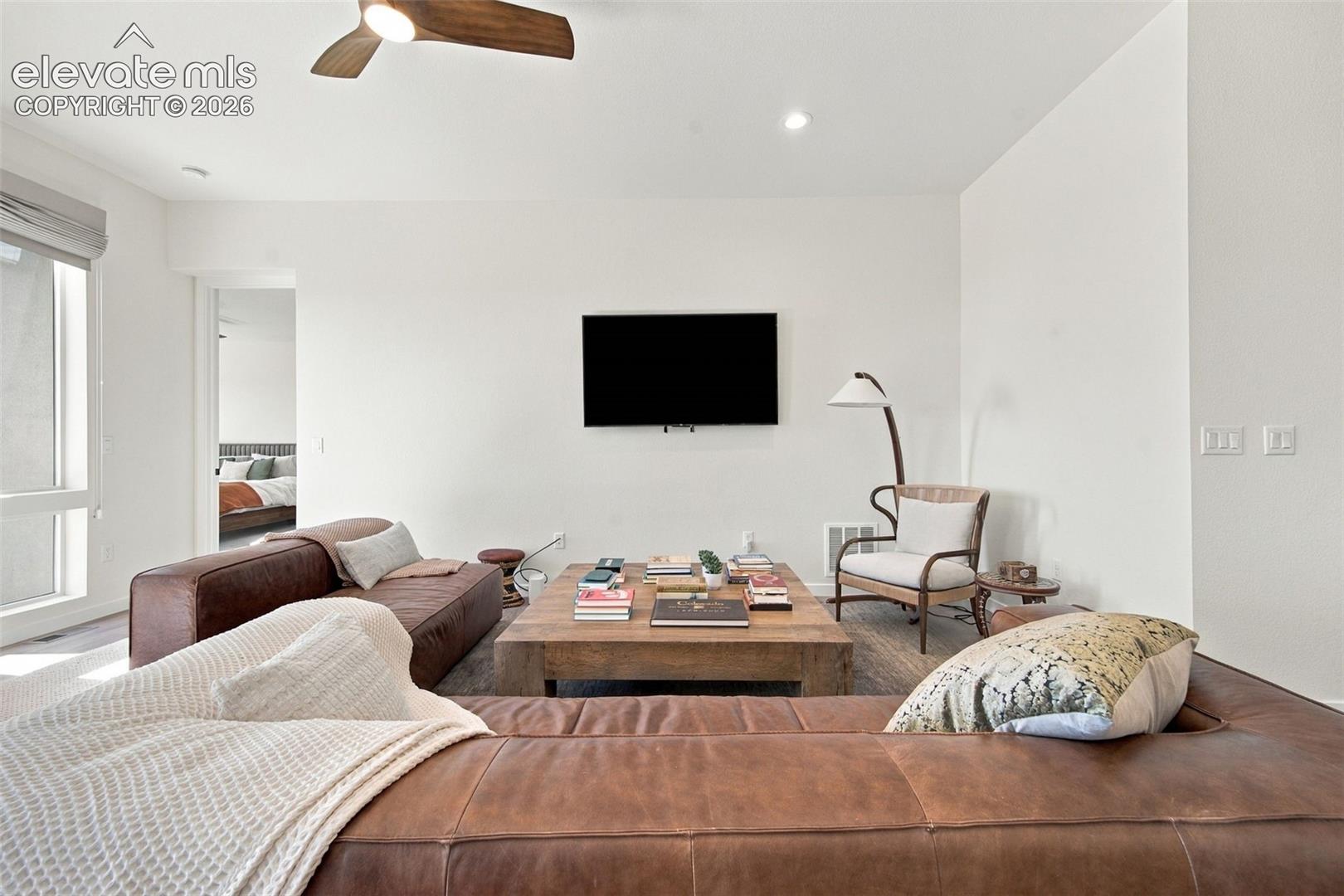 Living area featuring recessed lighting, a ceiling fan with wood-finish blades, and large windows