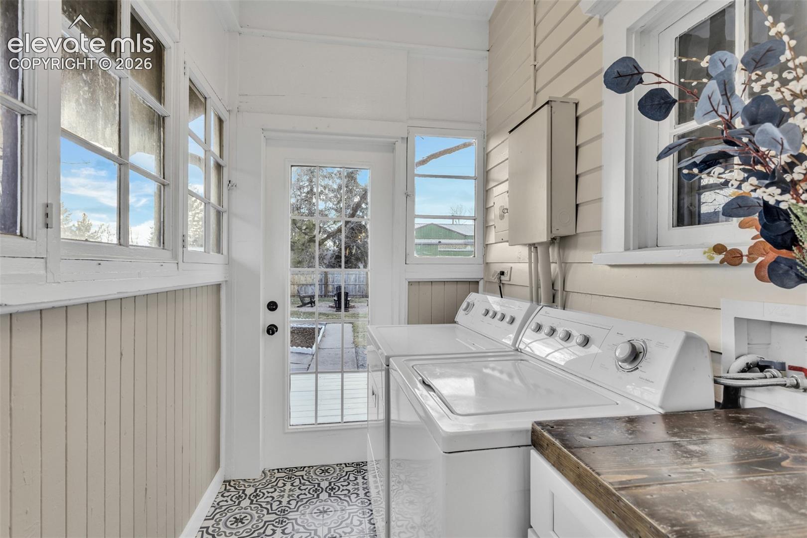 Laundry area featuring patterned floor tiles, beadboard wainscoting, multi-pane windows, and a glass-paned exterior door