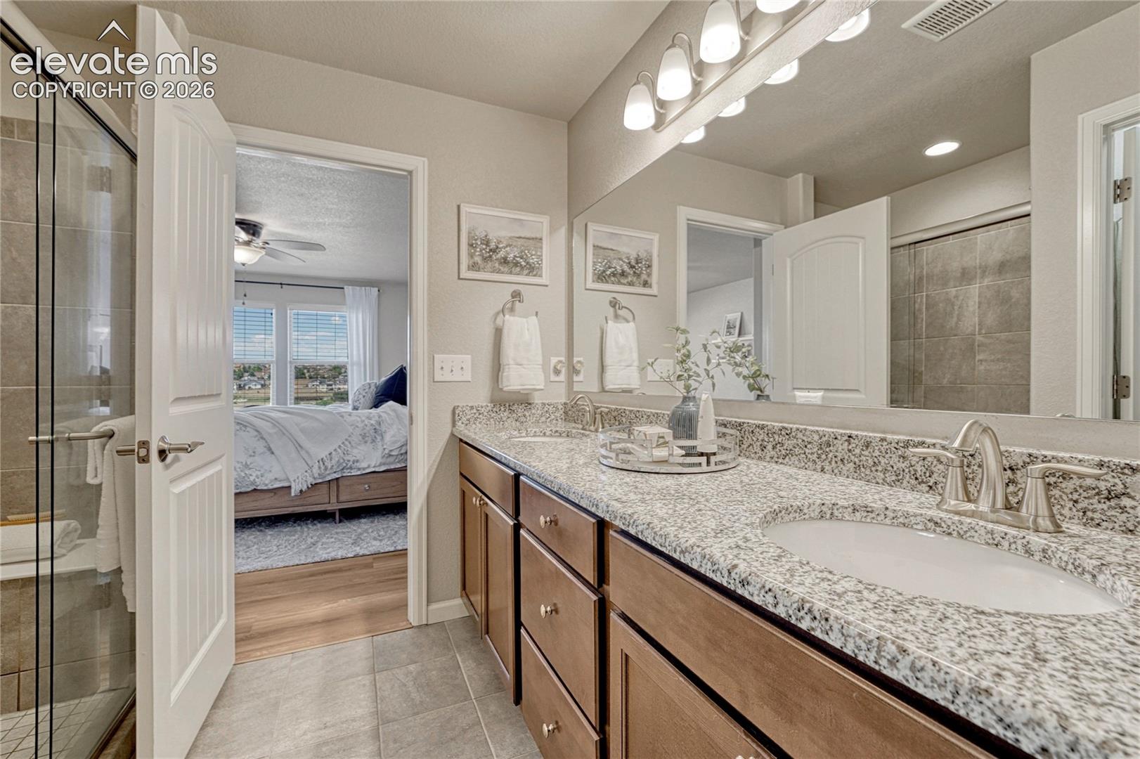 The primary bathroom offers a spa-like feel with dual sinks, granite countertops, ceramic tile flooring, and a spacious walk-in shower.