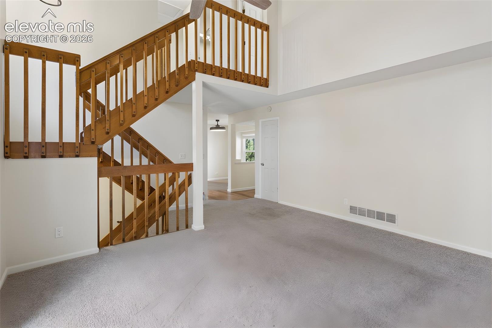 Different angle of living room with vaulted ceilings, and wood-finish staircase.