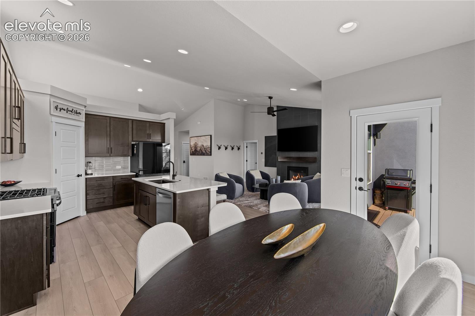 Open-concept space featuring dark wood-finish cabinetry, a central island with a stone-finish countertop, recessed lighting, wood-finish flooring, and a fireplace with a floor-to-ceiling tile surround