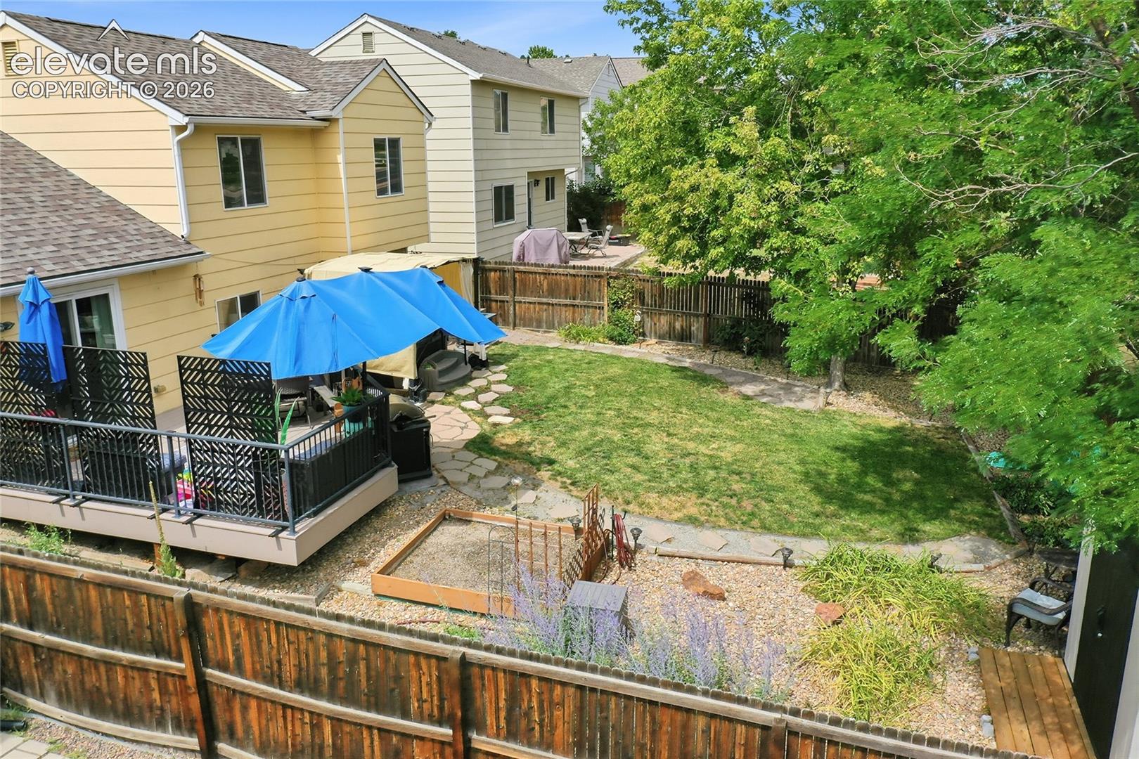 Elevated deck with metal railing, stone-pathway landscaping, wood-panel fencing, and established trees
