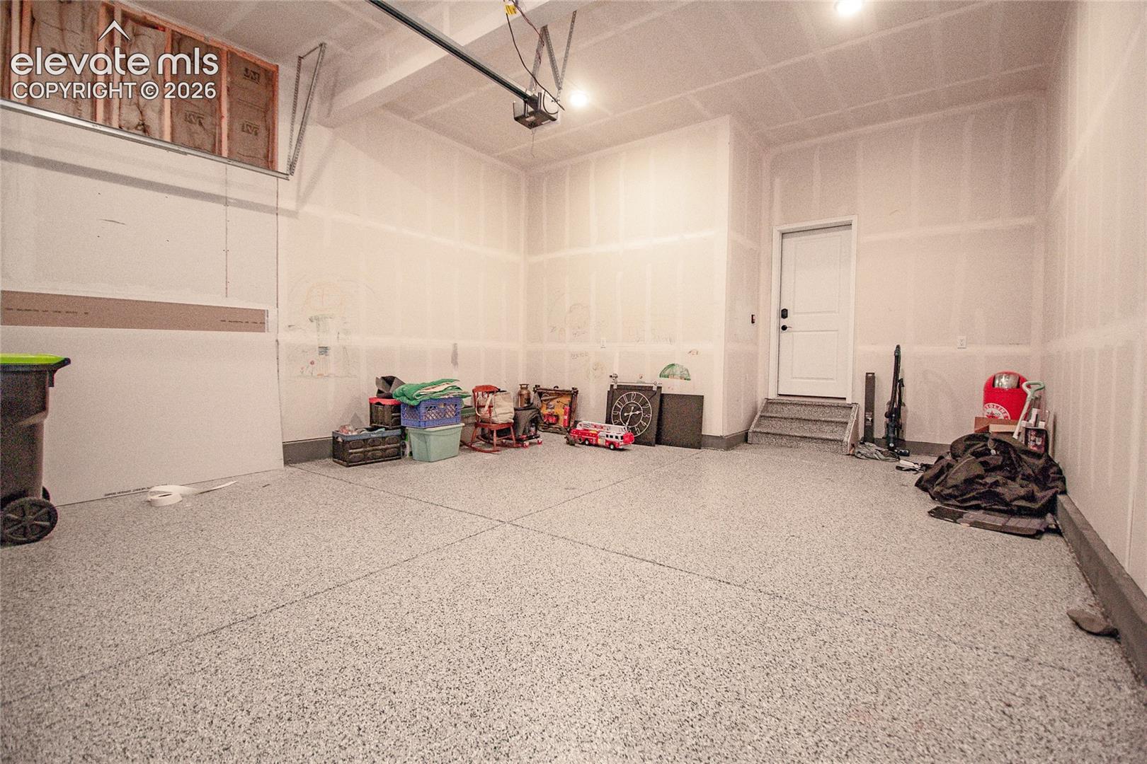 Finished garage featuring epoxy-coated flooring, painted drywall, recessed ceiling lighting, and a solid-core entry door with steps