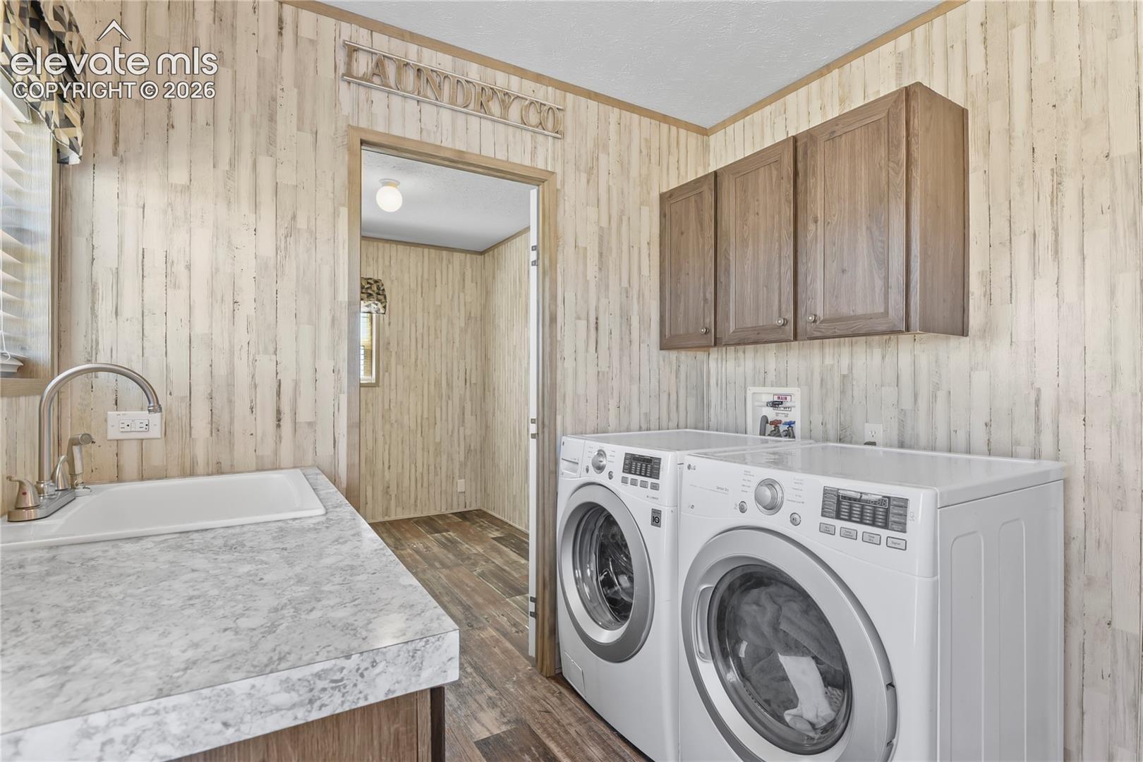 Laundry area featuring wood-finish paneling, drop-in utility sink with high-arc faucet, solid-surface countertop, and wall-mounted wooden cabinetry