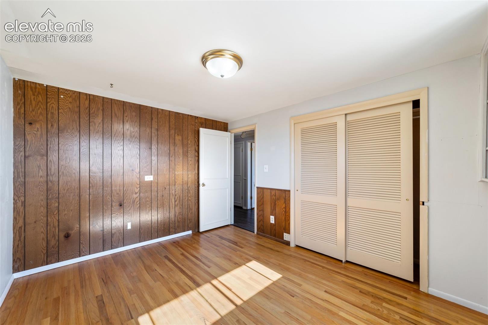 Room featuring wood-finish flooring, a wood-paneled accent wall, neutral wall paint, and a semi-flush mount ceiling light
