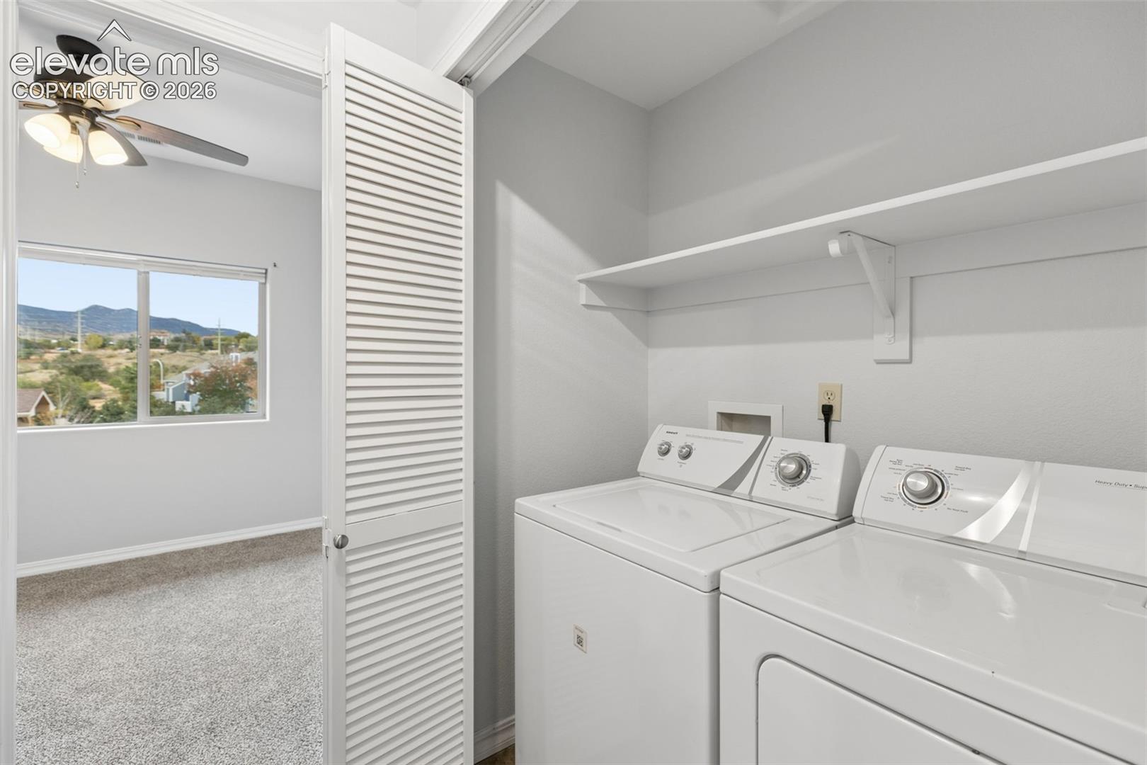 Laundry area featuring louvered bifold doors and built-in shelving, complemented by a room with carpeted flooring, a ceiling fan, and mountain scenery
