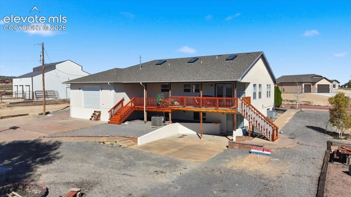 Exterior featuring a wood deck with stairs, three roof skylights, a concrete patio, and an auxiliary structure
