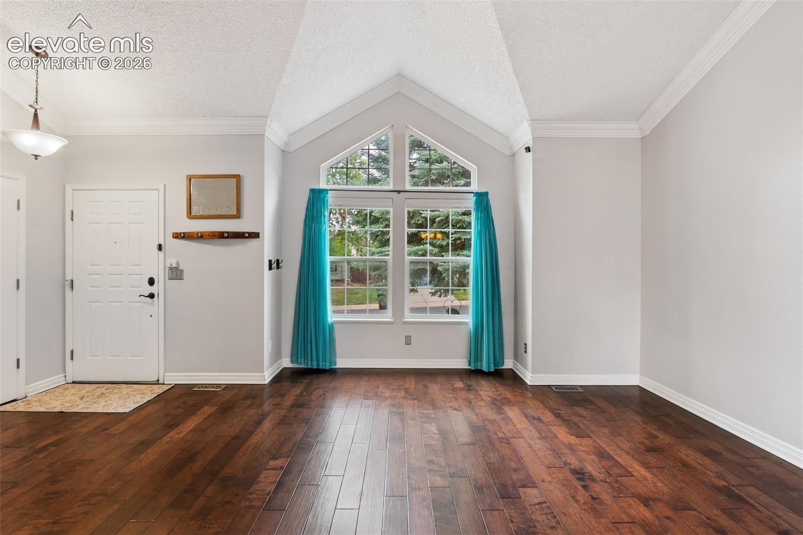 Vaulted ceiling with an architectural window, dark wood-finish flooring, and crown molding