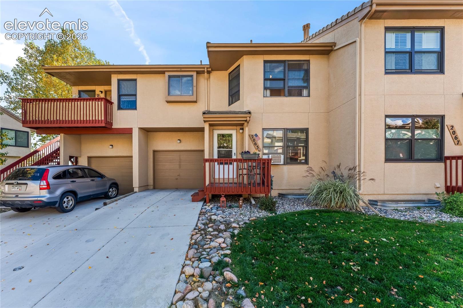 Stucco exterior featuring multiple windows with dark trim, a red-toned wood railing balcony, and a red-toned wood railing porch
