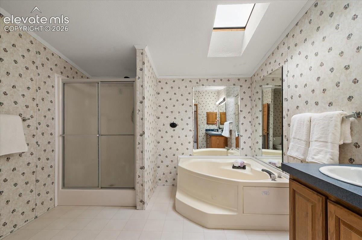 Corner soaking tub, skylight, walk-in shower with sliding frosted doors, full-width vanity mirror, and wood cabinetry