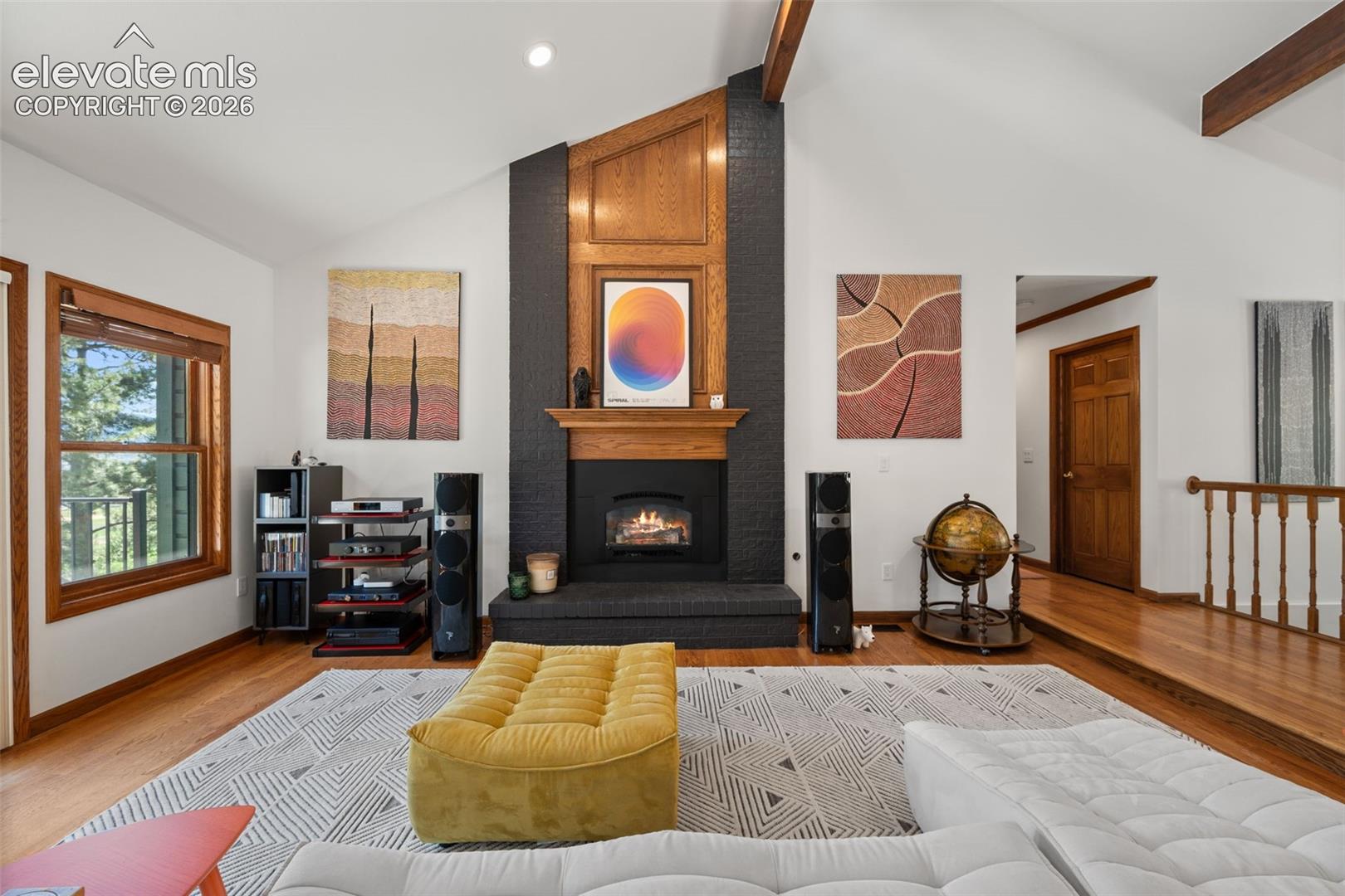 Vaulted ceiling living space featuring a black brick fireplace, wood mantel, and hearth