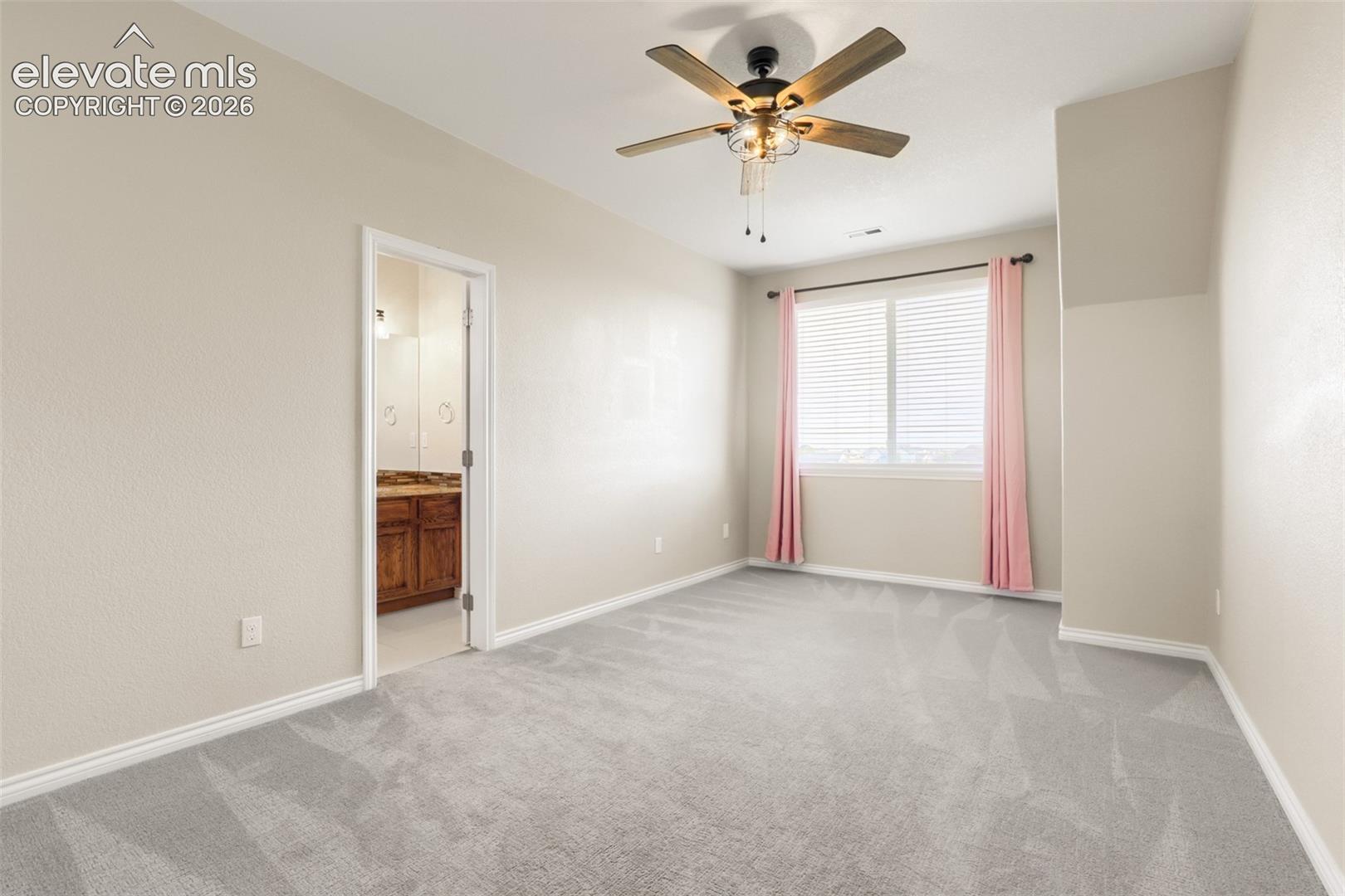 Desirable upper-level end suite featuring wall-to-wall carpet, warm neutral paint, and an updated wood-blade ceiling fan. Highlighted by a bright window for ample light, this private bedroom includes a dedicated walk-in closet and seamless access to its own private bathroom—offering convenience and privacy.