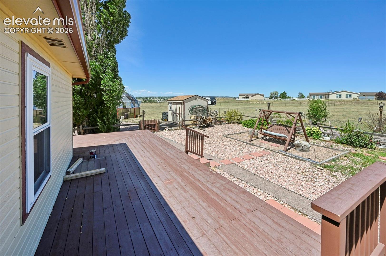 Expansive wood deck with railing, gravel ground cover, and a detached shed