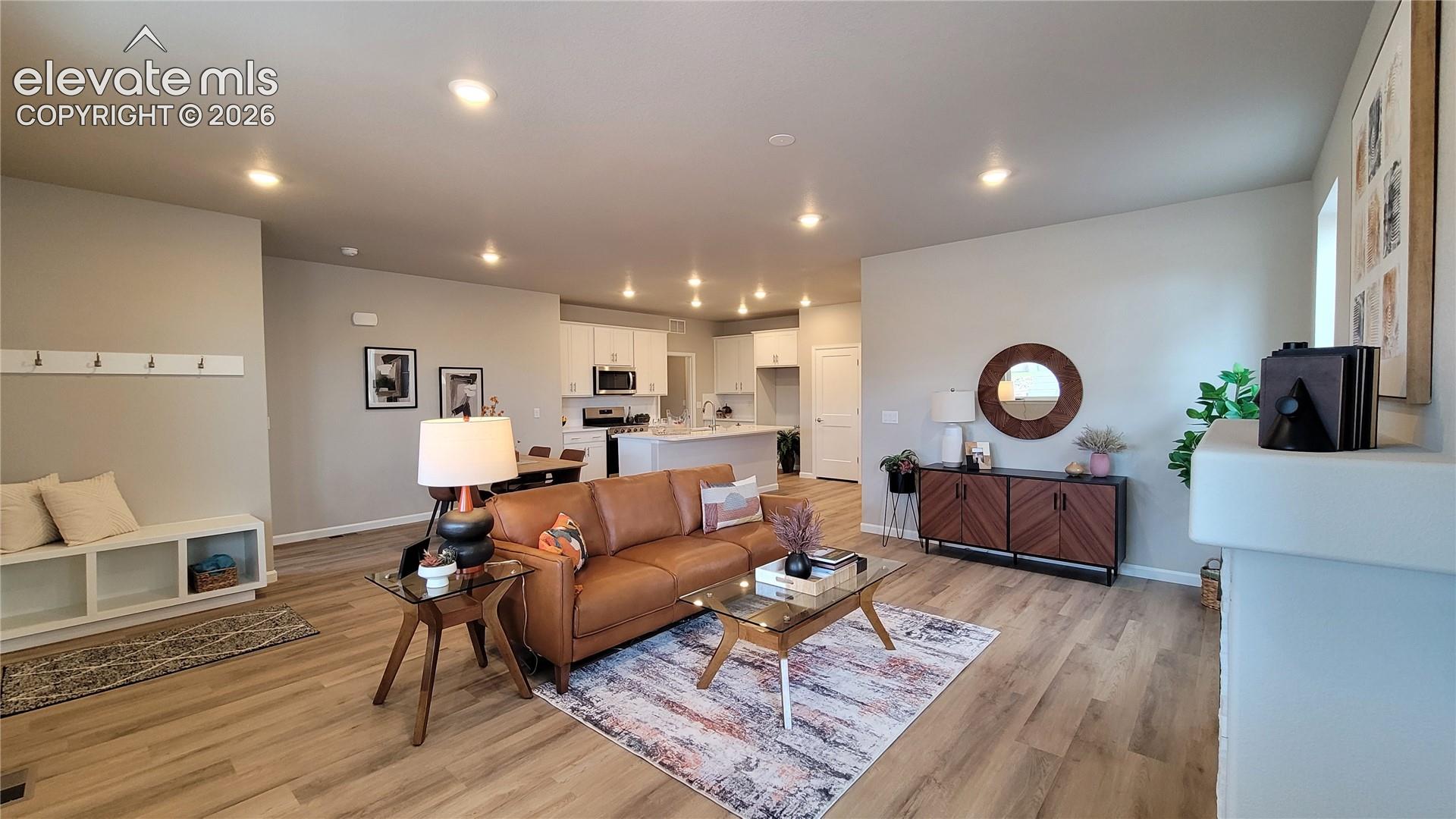 Open-concept interior featuring LVP flooring, recessed LED lighting, white cabinetry, a kitchen island, and a built-in wall bench