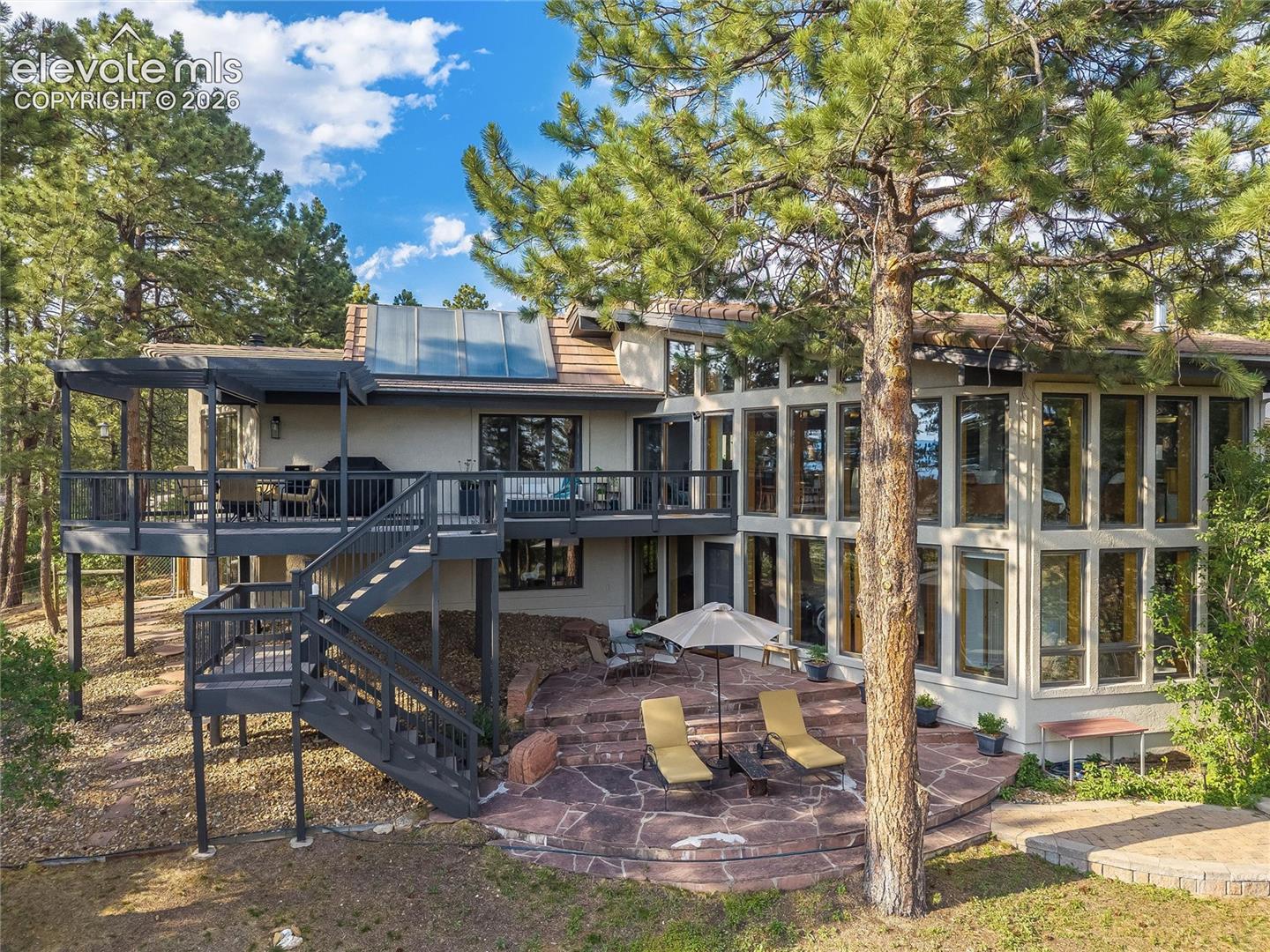 Multi-level exterior featuring extensive window arrays, a spacious elevated deck with a pergola, and a flagstone patio with stone steps