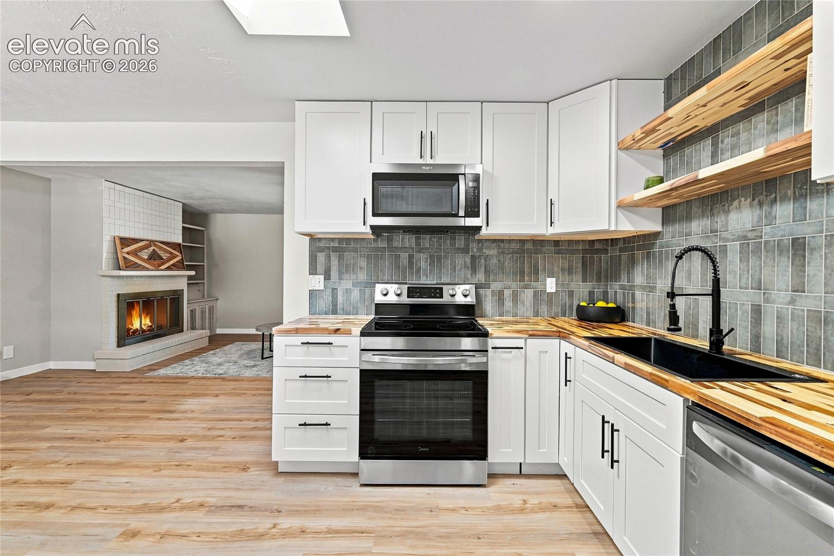 Contemporary kitchen featuring white cabinetry, wood-finish countertops, stainless steel appliances, and a tiled backsplash