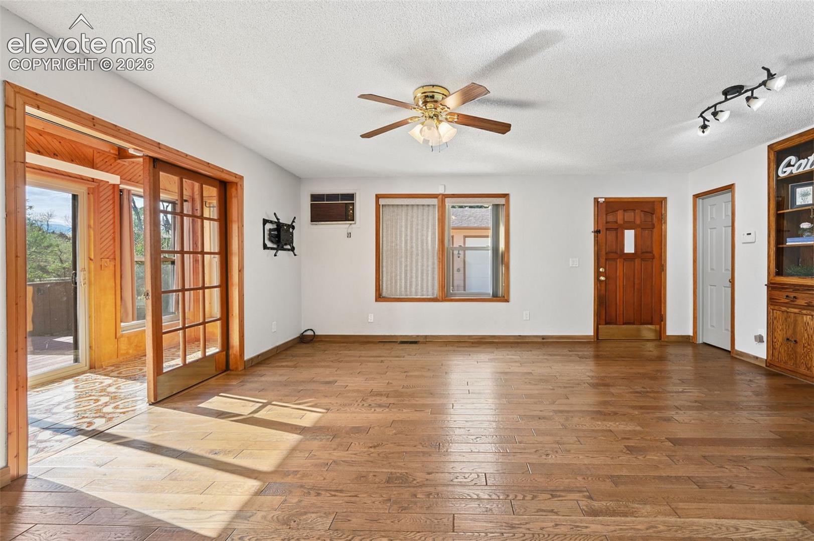 Living area featuring wood-finish flooring, built-in wooden cabinetry, recessed multi-directional lighting, ceiling fan, and French-style glass sliding doors