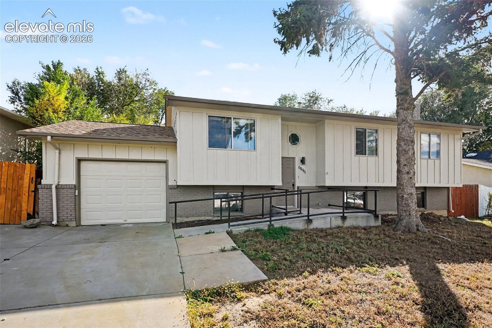 Split-level exterior featuring vertical siding, brick lower-level masonry, a concrete driveway, an attached garage, and a concrete entrance ramp with metal handrails