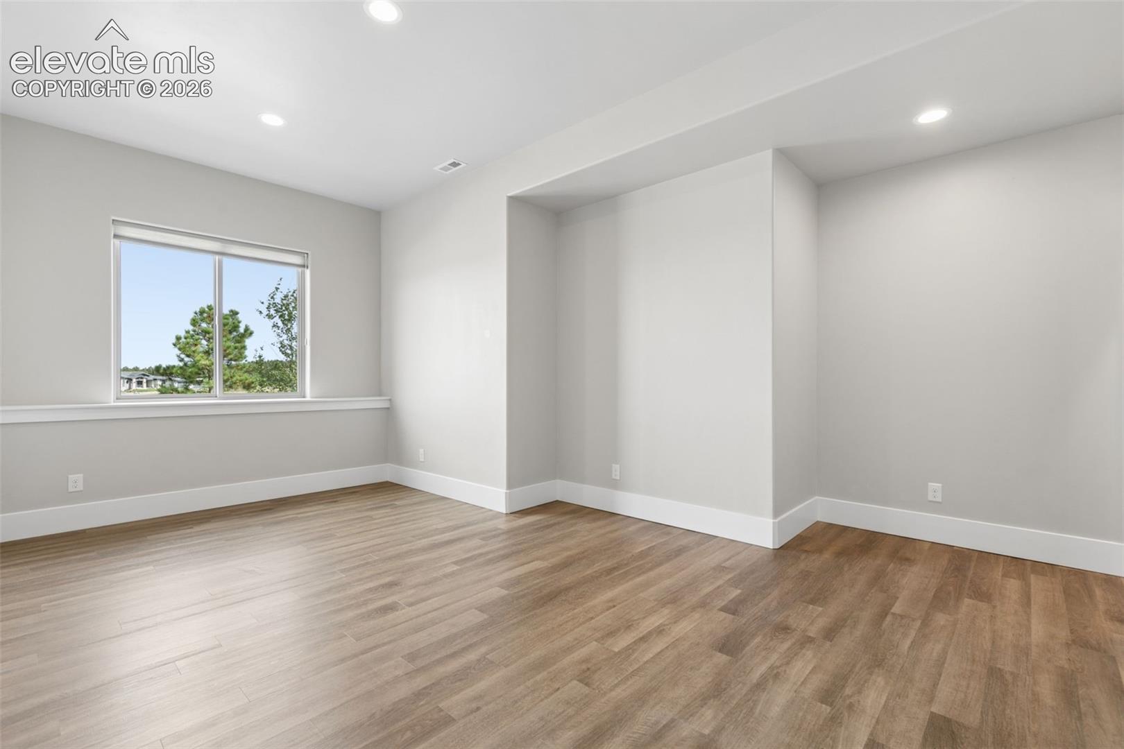 Recessed ceiling lights, wood-finish flooring, white trim, and a window with a white frame
