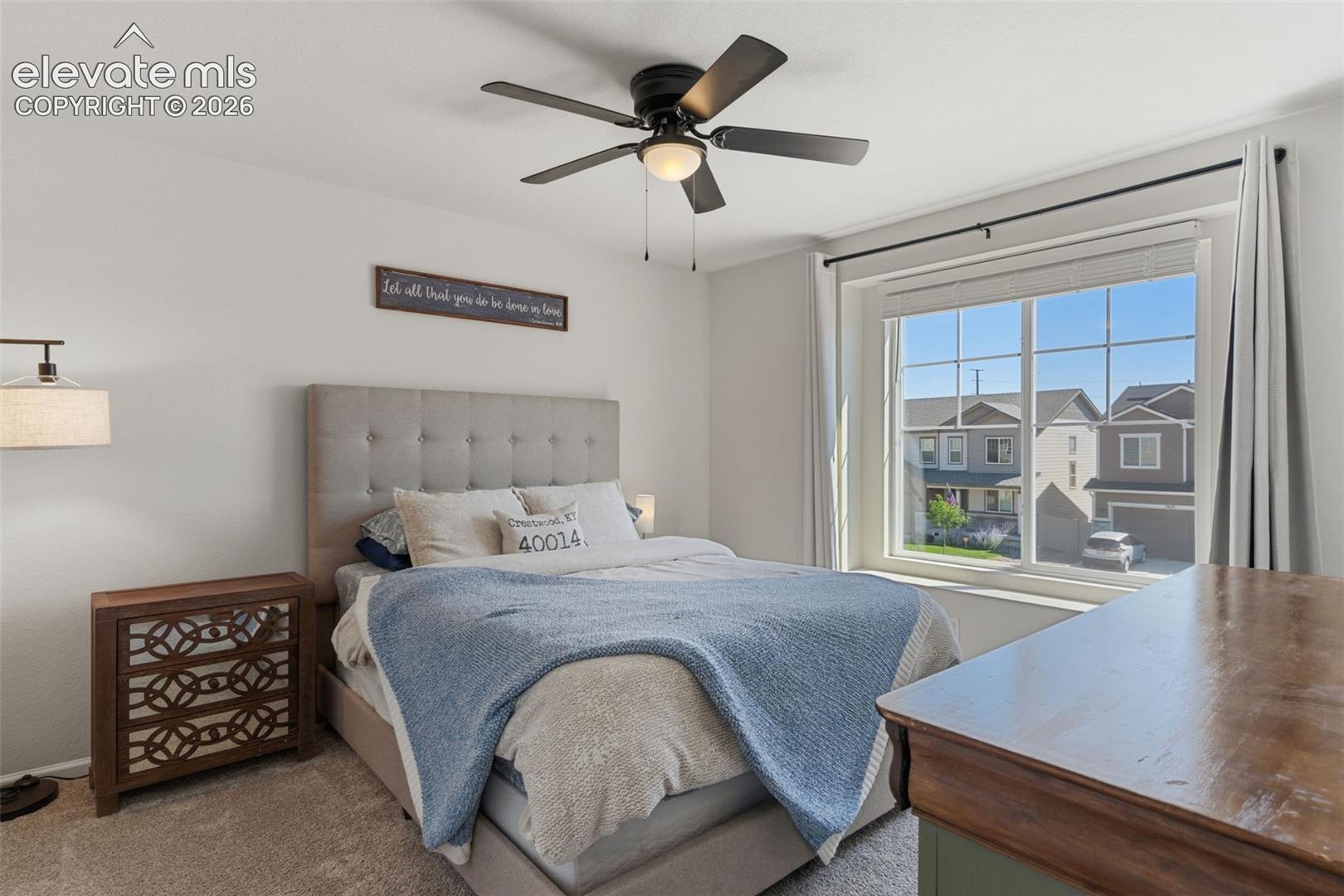 Bedroom featuring a large window, a ceiling fan with integrated lighting, and neutral carpeting