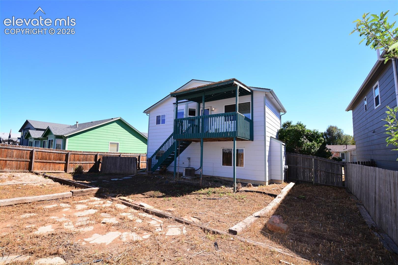 Rear exterior featuring a covered deck with railings, exterior stairway, and a privacy fence