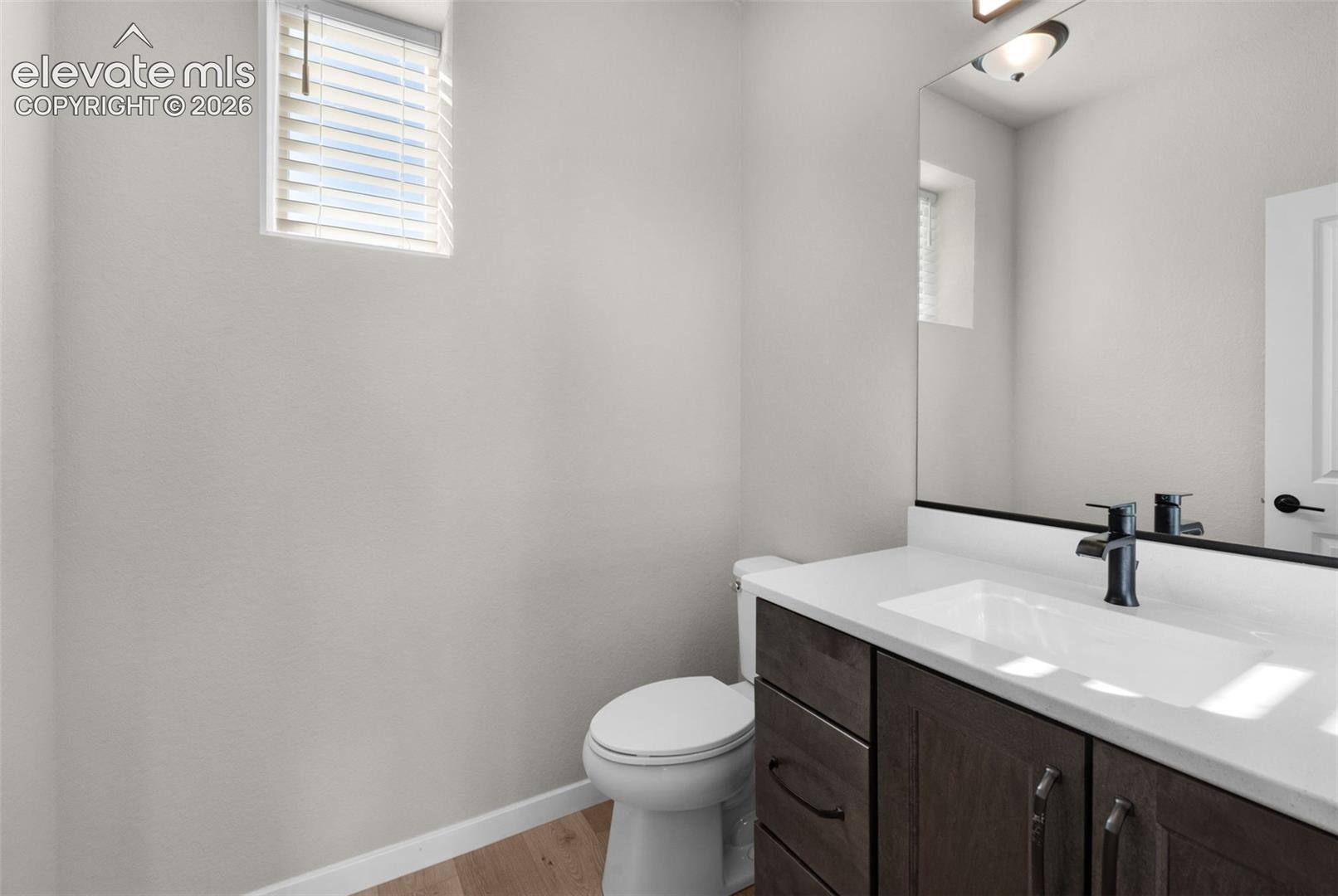 Powder room featuring a single vanity with a white countertop, dark wood-finish cabinetry, matte black faucet, and a toilet