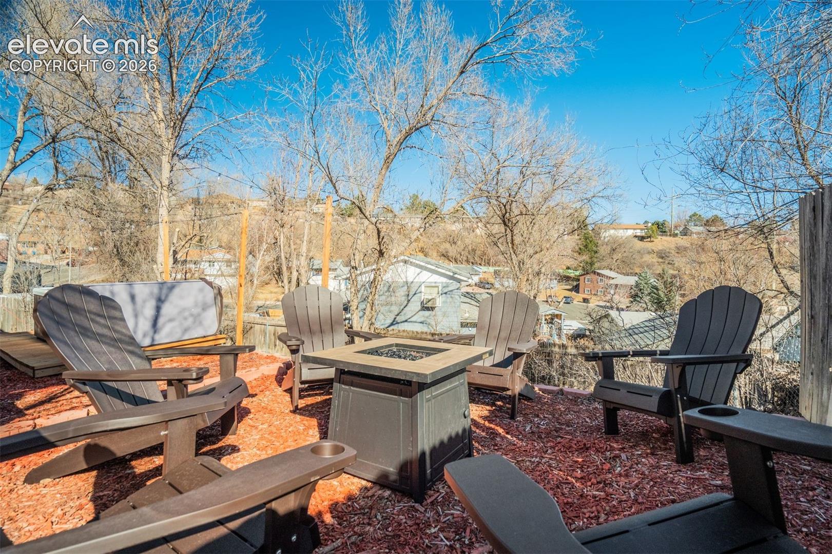 Outdoor patio area with a built-in fire pit, multiple Adirondack-style chairs, and a hot tub
