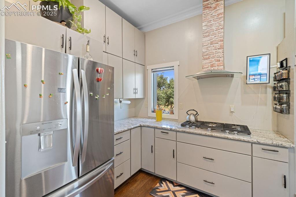 Kitchen with appliances with stainless steel finishes, wall chimney range hood, white cabinetry, dark wood-style flooring, and ornamental molding