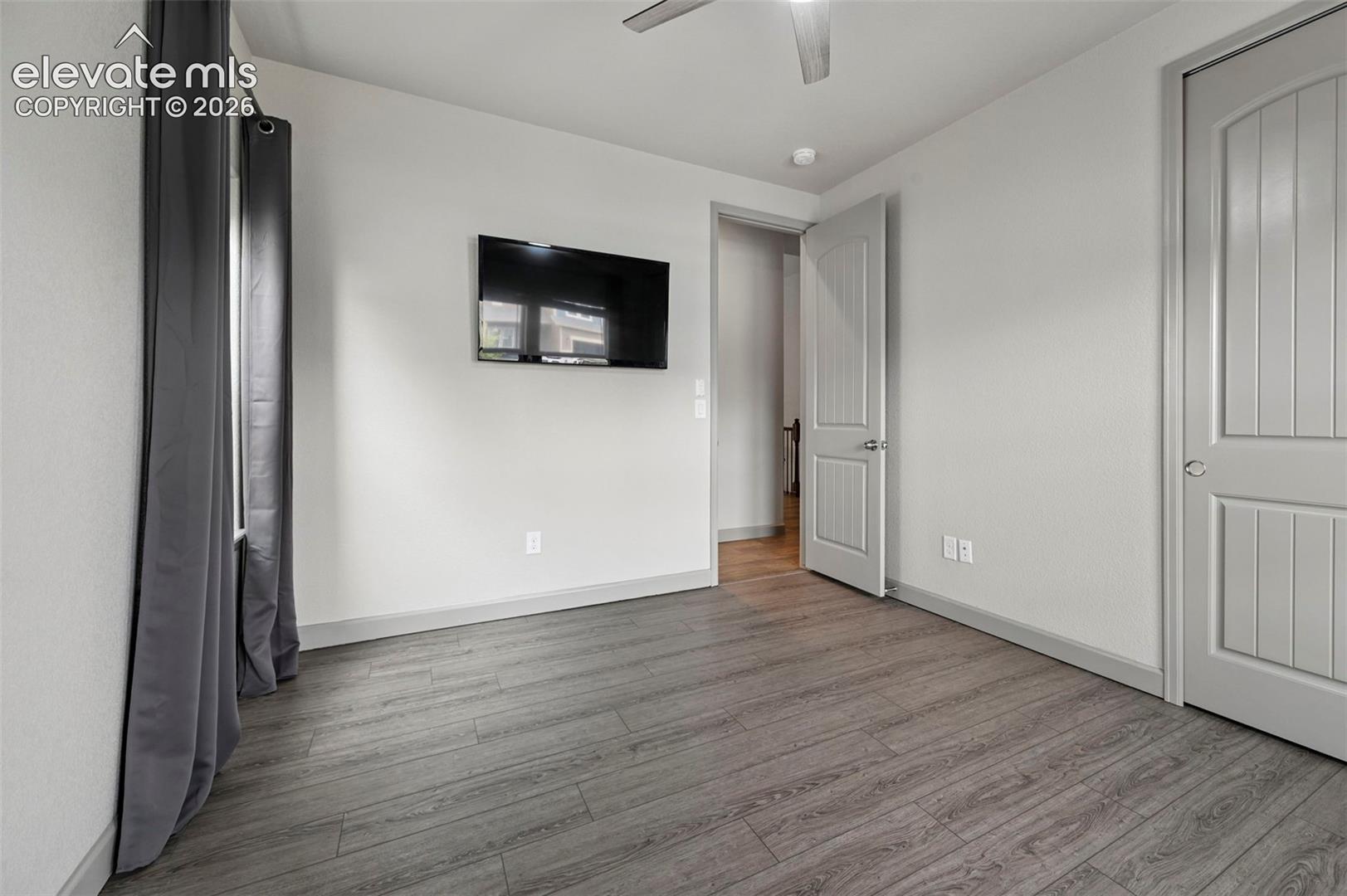 Wood-finish flooring, neutral wall tones, arched-panel interior door, and ceiling-mounted fan